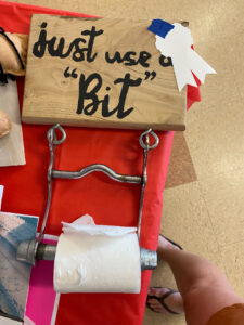 A horse bit with toilet paper, attached to wood that reads "Just use a 'Bit'".